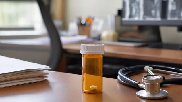 An amber prescription pill bottle with a single tablet sits on a wooden clinic desk beside a stethoscope, with brain-scan films softly out of focus in the background.