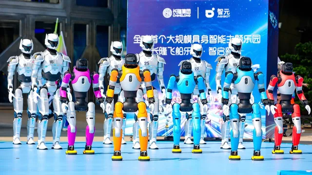 A row of white and multicoloured AGIBOT humanoid robots standing on a blue stage in front of a Chimelong and AGIBOT launch backdrop at the Chimelong Spaceship Park announcement.