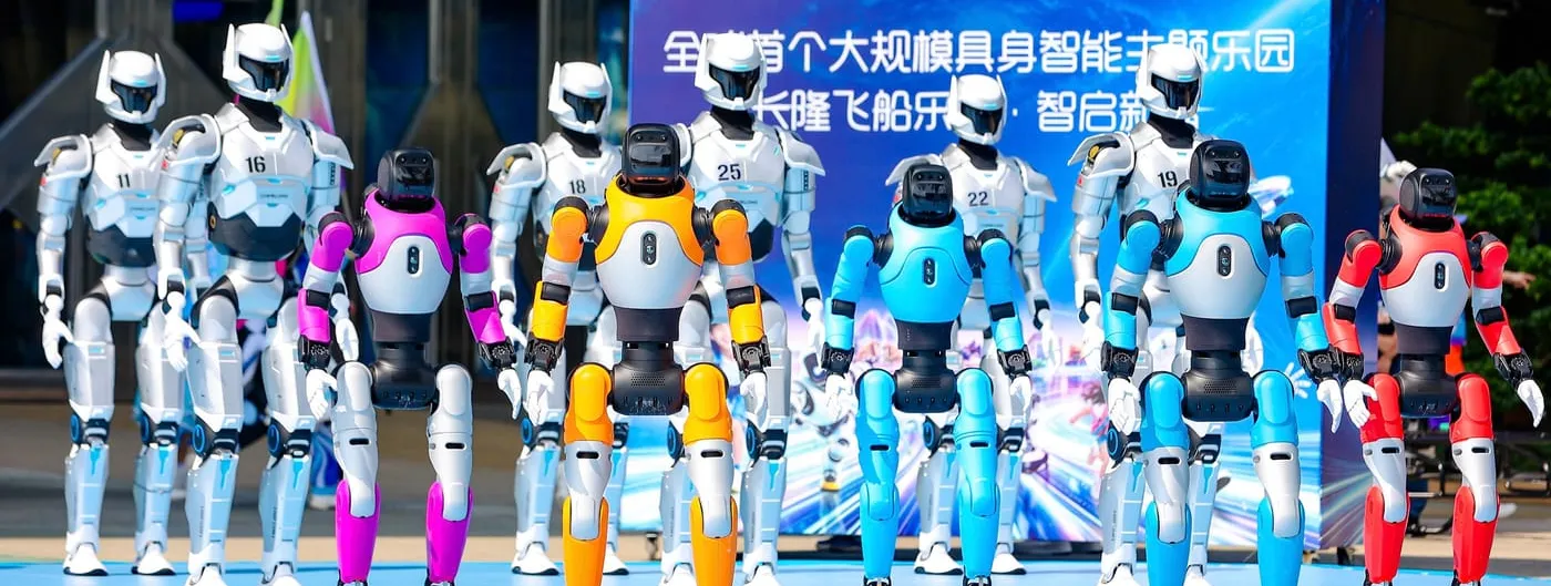 A row of white and multicoloured AGIBOT humanoid robots standing on a blue stage in front of a Chimelong and AGIBOT launch backdrop at the Chimelong Spaceship Park announcement.