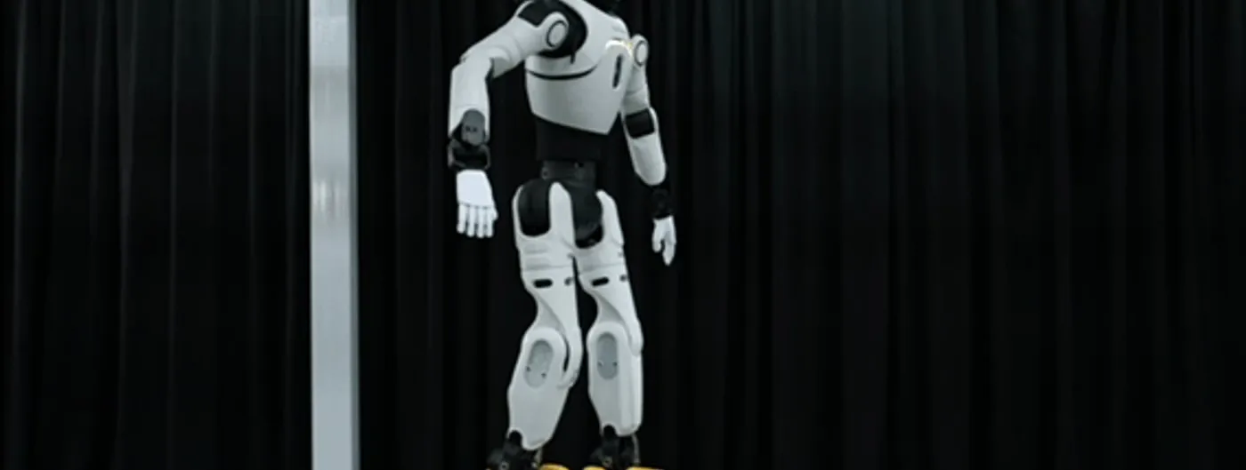 The white and black Lingxi X2 humanoid robot stands balanced on top of a large black ball in a studio, arms held out to the sides, with branded boxes stacked on the floor behind it.