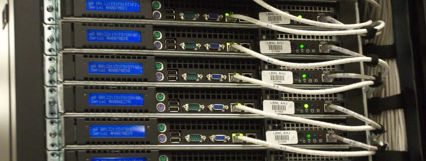 Close-up of the rear of a server rack in a data centre, showing cabling and small blue status displays.