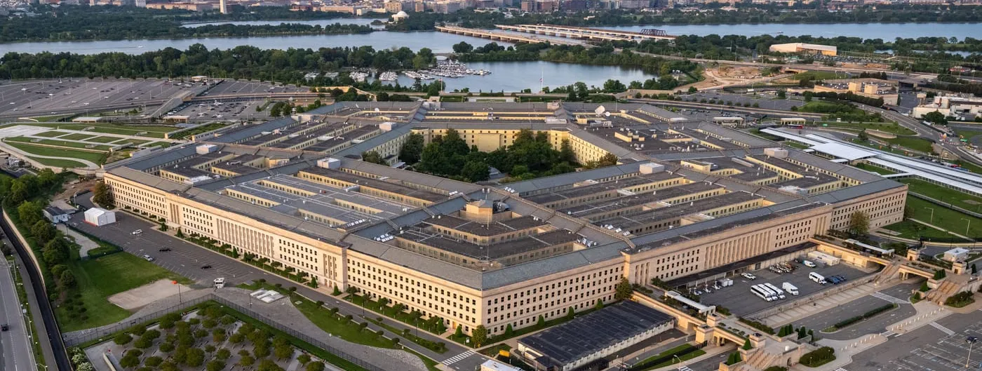 Aerial photograph of the Pentagon building in Washington, D.C., with the Potomac River, Washington Monument and U.S. Capitol visible in the background.