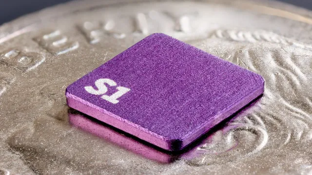Sonera's purple S1 magnetometer chip, engraved with its "S1" label, resting on the ridged edge of a coin to show its actual small size.