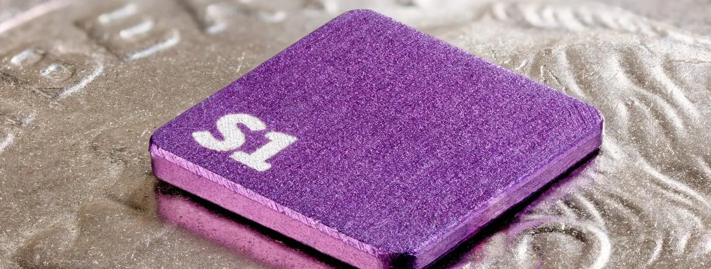 Sonera's purple S1 magnetometer chip, engraved with its "S1" label, resting on the ridged edge of a coin to show its actual small size.