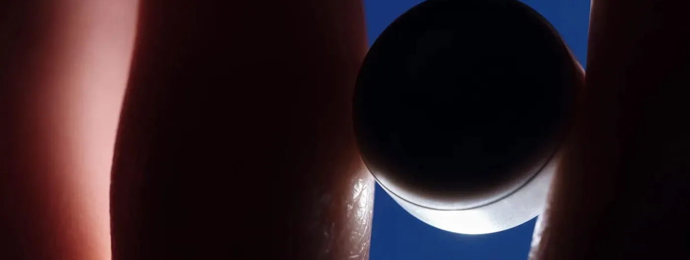 A small dark disc-shaped electronic device held between two fingertips, silhouetted against a deep blue sky.