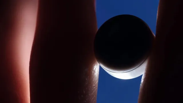 A small dark disc-shaped electronic device held between two fingertips, silhouetted against a deep blue sky.