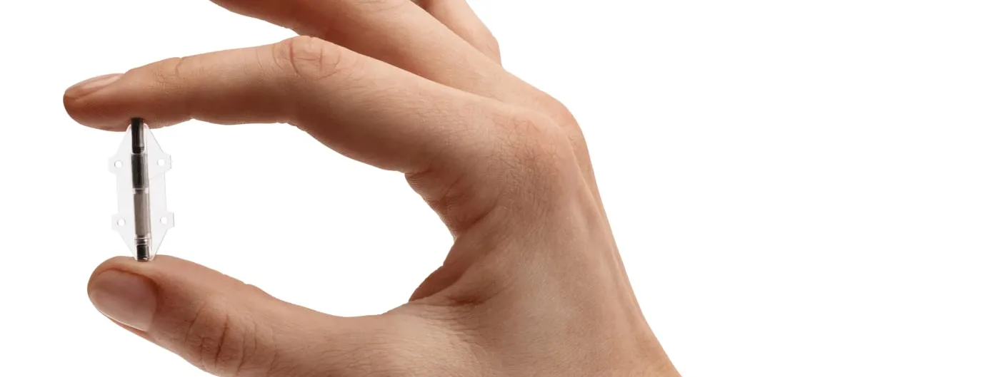 A hand holds a slim metal implant the length of a fingernail between thumb and forefinger against a white background.