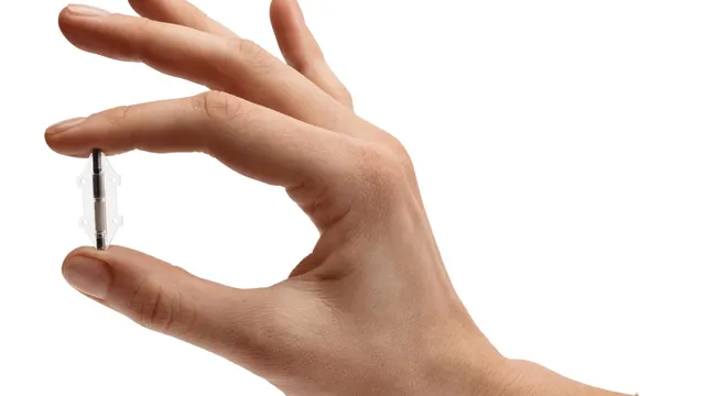 A hand holds a slim metal implant the length of a fingernail between thumb and forefinger against a white background.