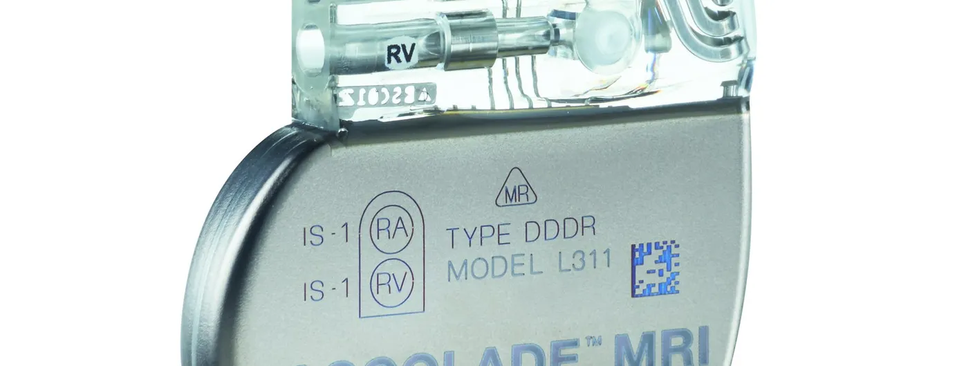 A titanium-cased dual-chamber pacemaker photographed against white, its clear epoxy header showing two lead ports marked RA and RV above the engraved device model text.