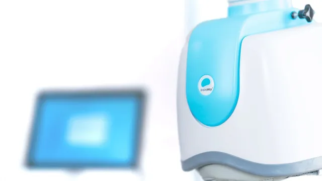 A white and pale blue transcranial magnetic stimulation helmet unit on its positioning arm, with a blurred treatment screen beside it.