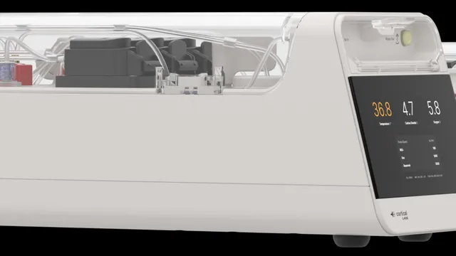 Two Cortical Labs CL1 units side by side, low white enclosures with transparent upper covers showing tubing and circuit boards, the front unit's panel reading a temperature of 36.8 alongside carbon dioxide and oxygen values.