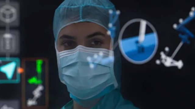 A surgeon in a blue surgical cap and mask looks toward the camera in a darkened operating theatre, with translucent navigation graphics and tracker markers overlaid across the foreground.