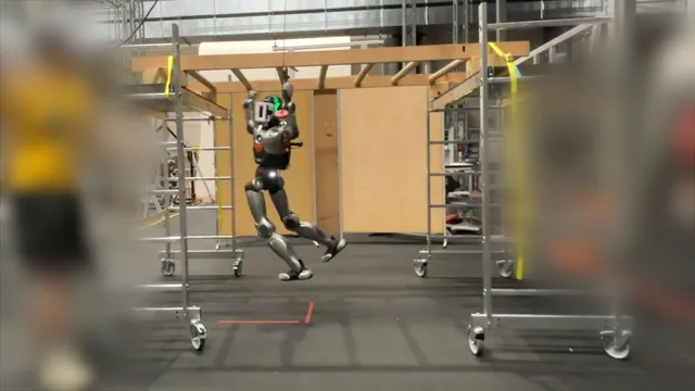 A silver humanoid robot hangs by both arms from a wooden overhead ladder in a laboratory, its legs swinging clear of the floor between two mobile scaffolding towers.