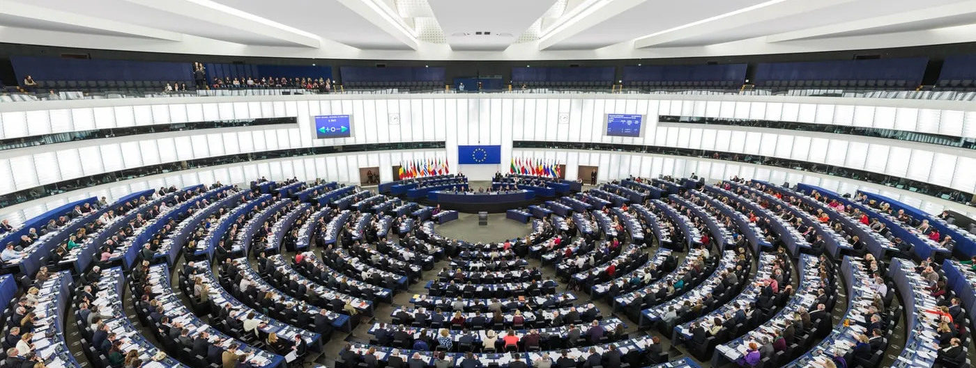 The semi-circular tiered chamber of the European Parliament in Strasbourg during a plenary session, with members seated in curved rows.