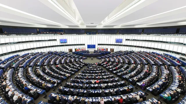 The semi-circular tiered chamber of the European Parliament in Strasbourg during a plenary session, with members seated in curved rows.