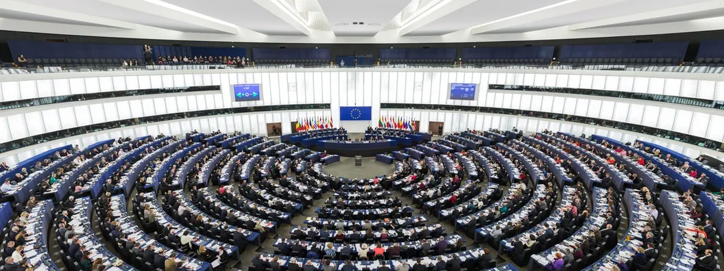 The semi-circular tiered chamber of the European Parliament in Strasbourg during a plenary session, with members seated in curved rows.