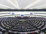The semi-circular tiered chamber of the European Parliament in Strasbourg during a plenary session, with members seated in curved rows.