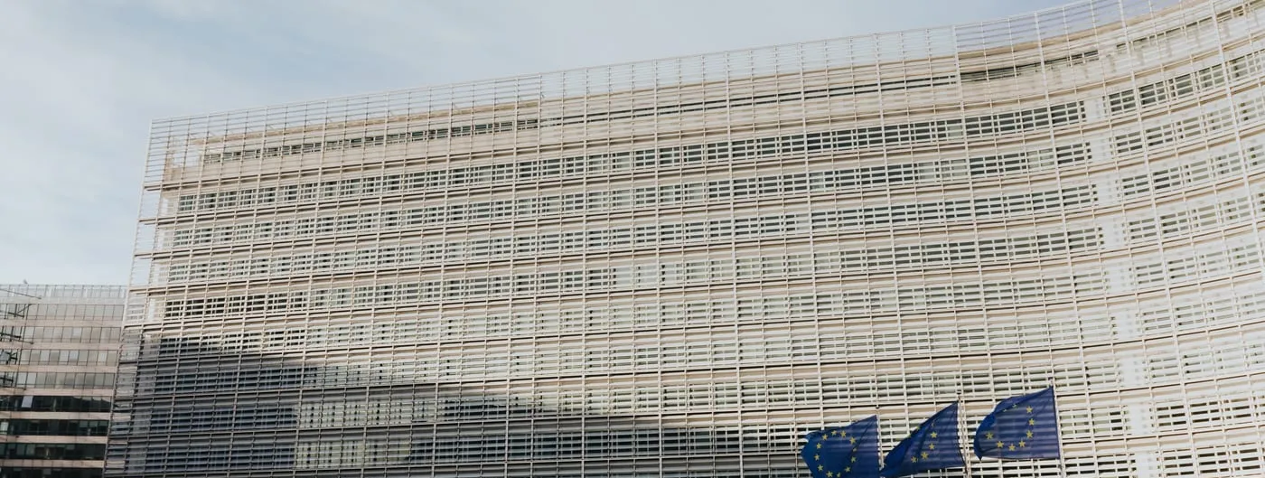 The Berlaymont building in Brussels, headquarters of the European Commission, its cross-shaped glass facade seen from the street with European flags in front.