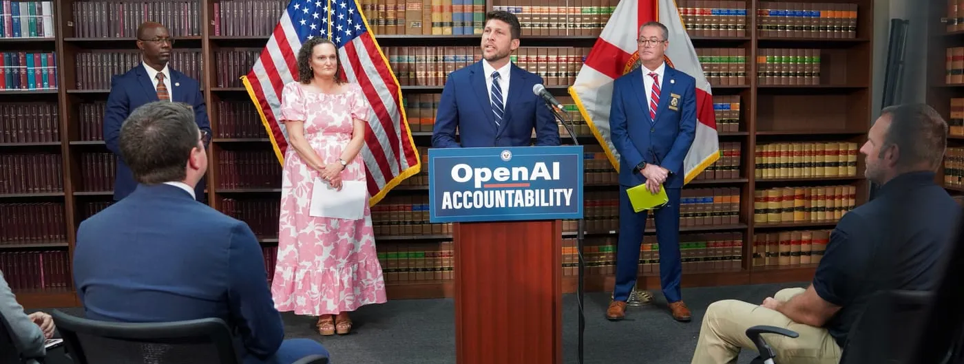 Florida Attorney General James Uthmeier speaks at a lectern marked OpenAI Accountability between a US flag and a Florida flag, at the June 2026 announcement of the state's lawsuit, in front of a wall of law books.