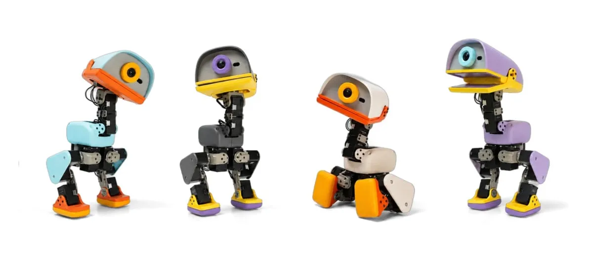 Four small two-legged robots with rounded duck-like heads and coloured panels in orange, grey, cream and purple, standing in a row on a white background.