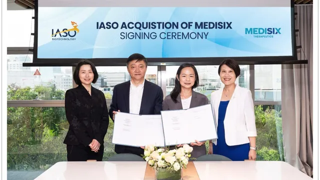 Four executives stand in a glass-walled meeting room holding open signed folders toward the camera, beneath a screen reading IASO Acquisition of MediSix Signing Ceremony with both company logos.