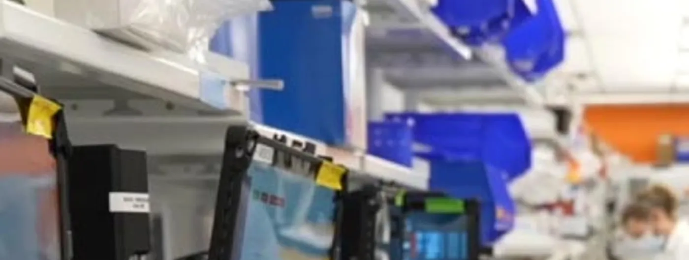 A laboratory interior at Intellia Therapeutics, with instrument touchscreens in the foreground, shelves of blue-lidded containers overhead, and a masked worker in a white coat at the back of the room.