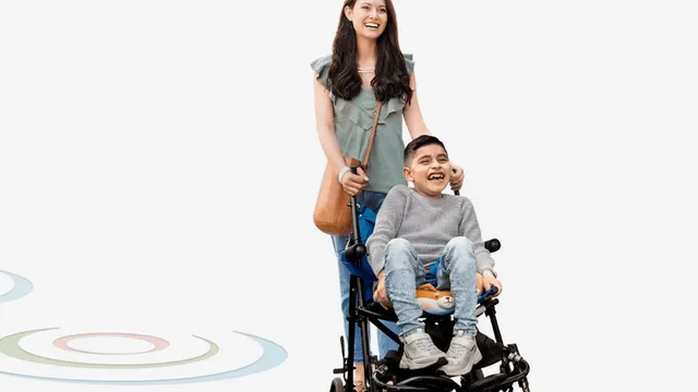A smiling mother pushes her laughing young son, who sits in an adaptive paediatric wheelchair.