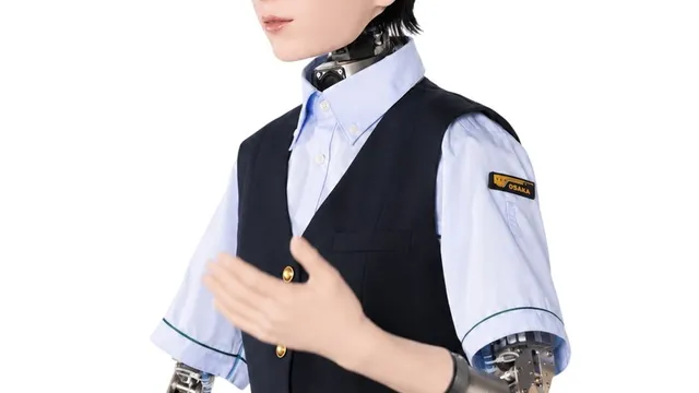 An android in a navy Osaka Metro waistcoat, pale blue shirt and peaked cap gestures with one hand, its exposed metal wrist and forearm mechanism visible below the rolled sleeve.