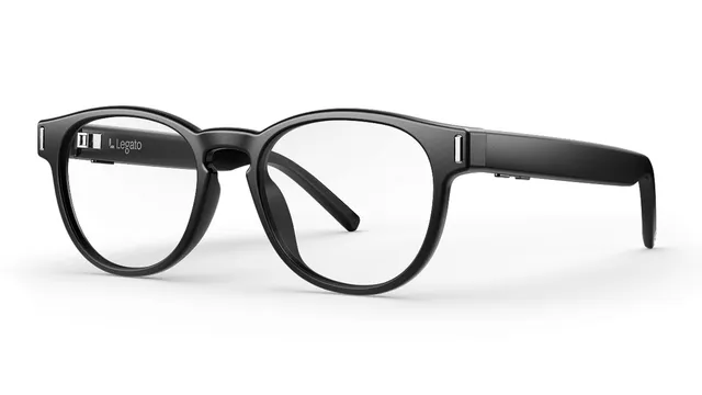 A three-quarter view of Legato black round-framed hearing glasses on a white background, showing the Legato mark and the small microphone and button details on the temple arms.