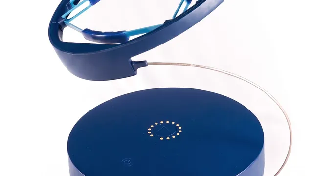 A navy-blue, lightweight head-worn magnetic therapy ring with light-blue internal contact pads, connected by a thin cable to a round tabletop console, photographed on a white studio background.