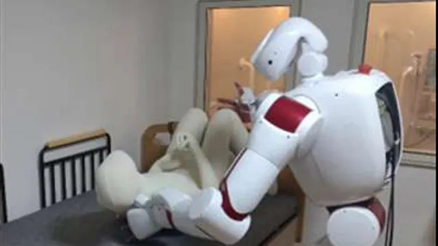 A white and red humanoid robot leans over a hospital bed, both arms under a pale mannequin, lifting it from lying flat towards a sitting position.