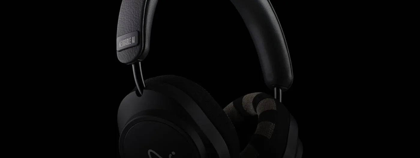 Black over-ear headphones with a leather headband and knit-fabric ear cushions, photographed in low-key lighting against a black background, with a Neurable AI plate on the headband.