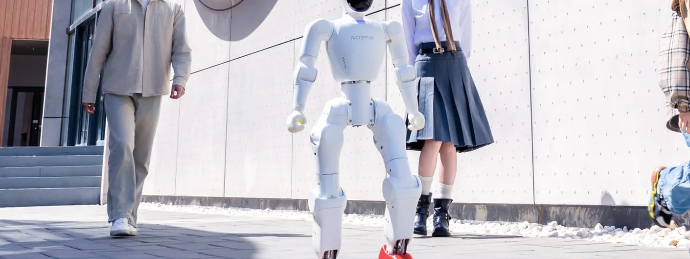 A white Noetix humanoid robot, its torso marked NOETIX, walks on a paved plaza between a man, a woman and a child outside the company headquarters.