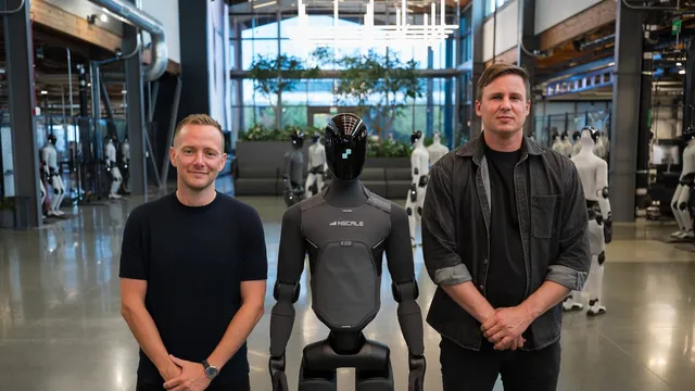 Two men in dark clothing stand on either side of a black humanoid robot wearing an Nscale-branded torso panel, inside a bright robotics facility with rows of other humanoids behind them.