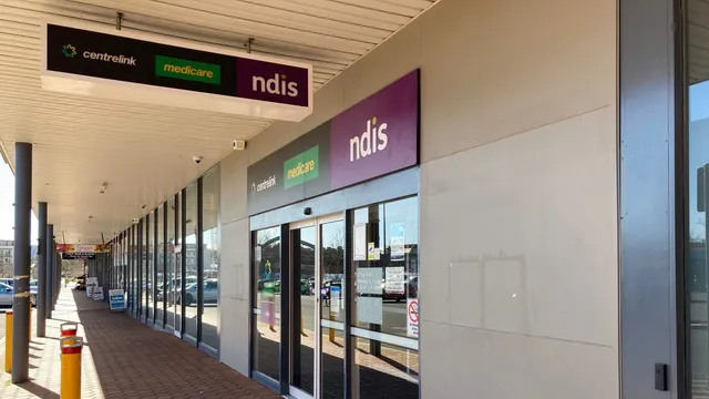 Storefront entrance of a Services Australia service centre in Canberra, with wall-mounted and hanging signs reading Centrelink, Medicare and NDIS above the glass doors.