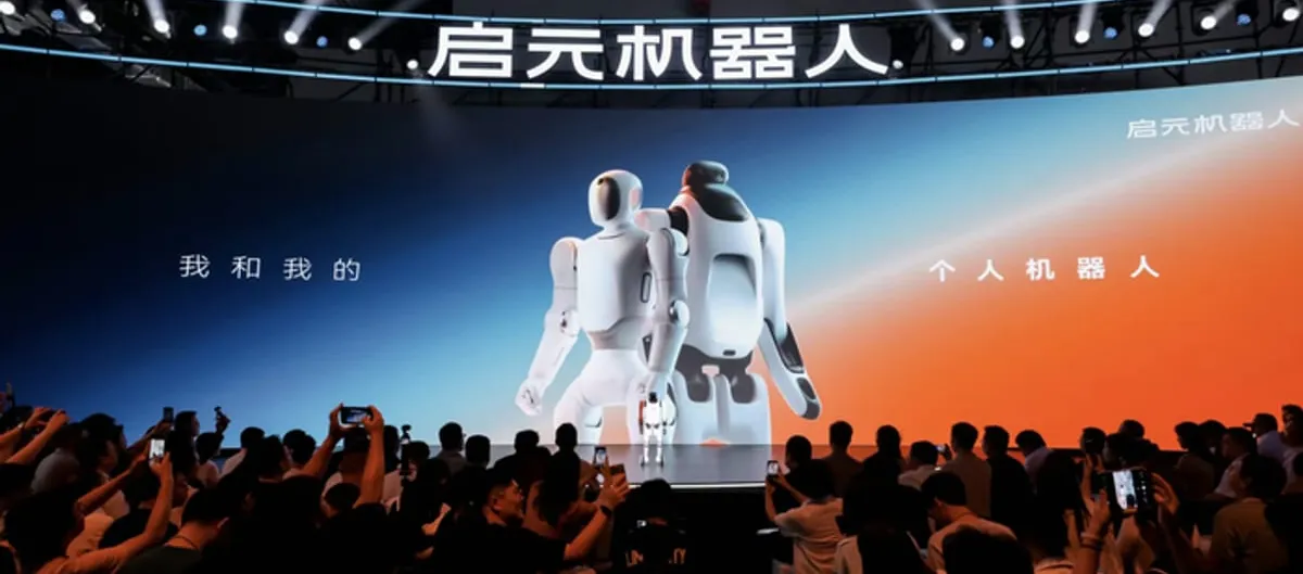 White Qiyuan Q1 and T1 robots standing side by side on a lit stage under a large "Qiyuan Robot" sign at the launch event, with a crowd filming on their phones.
