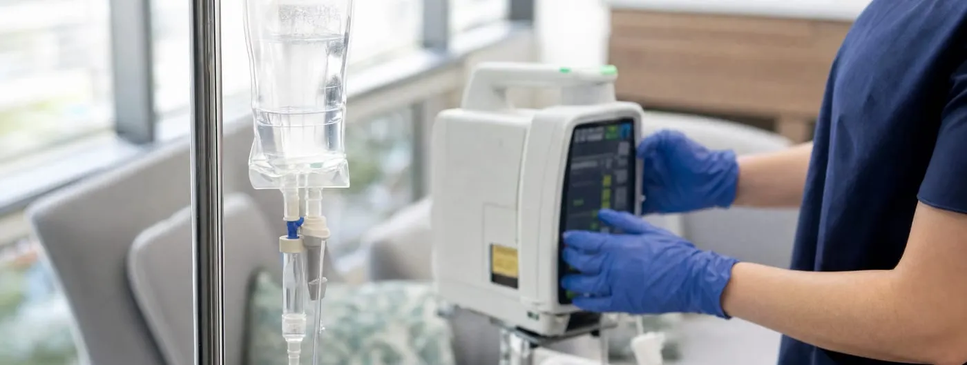 Photorealistic close-up of an IV infusion bag and pump with a nurse's gloved hands adjusting the pump controls, in a bright clinical room.