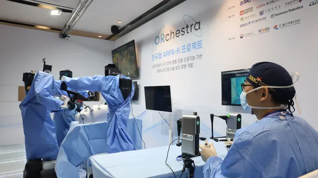 Two robotic arms draped in blue sterile covers work at an operating table while a masked surgeon watches an endoscope monitor, with the ORchestra project's partner signage on the wall behind them.