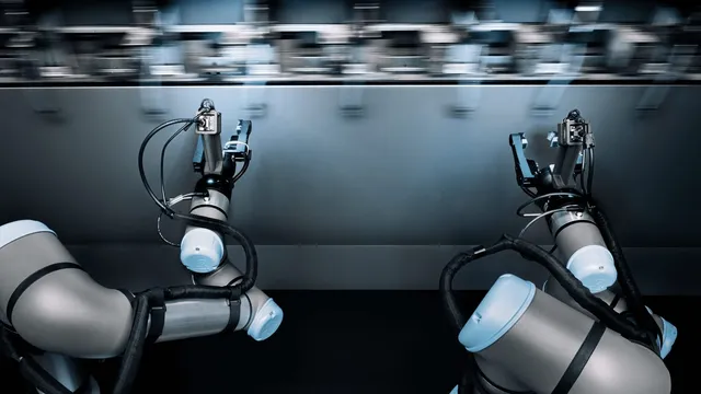 Two industrial robot arms fitted with grippers reach toward a production line that is blurred with motion behind them.