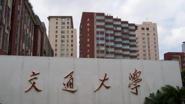 The white stone entrance wall of Shanghai Jiao Tong University, carrying the gold characters 交通大学, with the medical campus tower blocks rising behind it.