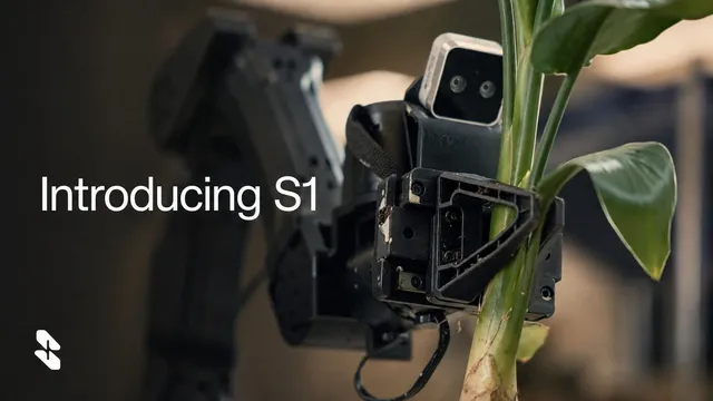 A black robotic gripper with an exposed camera module grasps the stem of a leafy green plant, a second robot arm blurred in the background of an indoor room, with the words Introducing S1 overlaid at left.