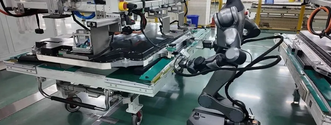 A grey Spirit AI Moz1 wheeled humanoid robot reaches into a CATL battery-pack conveyor line, its dexterous hand working among cables amid factory machinery on a teal factory floor.
