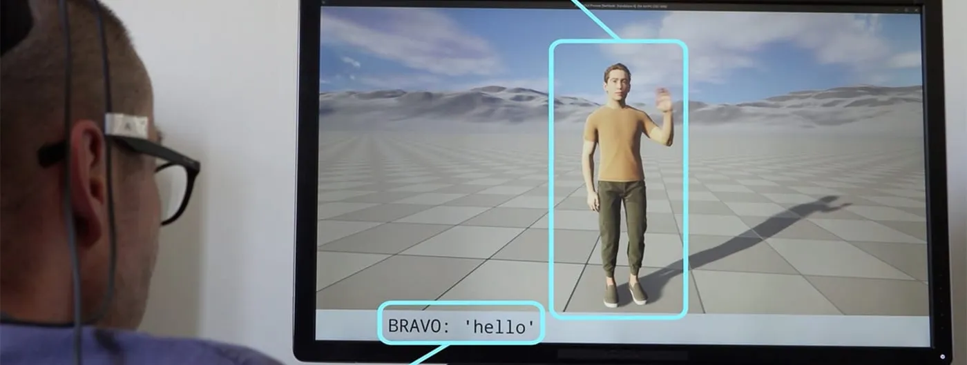 A study participant with an implanted electrode cable running from his head watches a monitor as a full-body virtual avatar raises its arm and displays the caption BRAVO: 'hello', with on-screen labels reading Decoded gesture from brain activity and Decoded speech from brain activity.