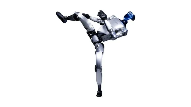 A silver bipedal humanoid robot with a dark visor balances on one leg with the other leg extended high in a kick, photographed against a plain white background.