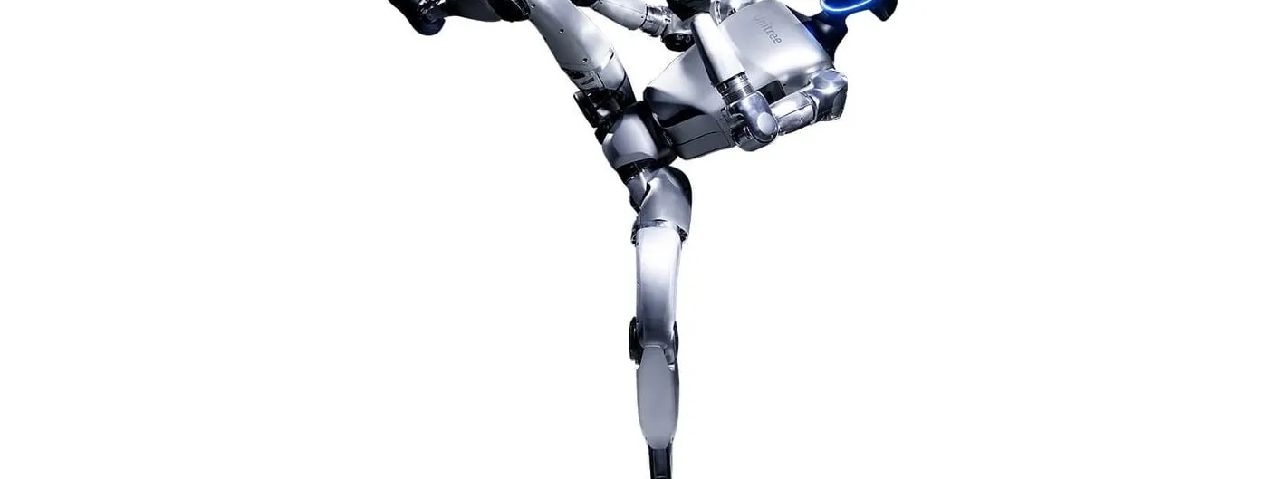 A silver bipedal humanoid robot with a dark visor balances on one leg with the other leg extended high in a kick, photographed against a plain white background.