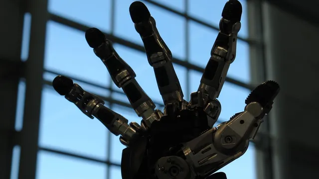 A five-fingered anthropomorphic robotic gripping hand with a pale casing, held palm-forward and mounted on a mechanical wrist.