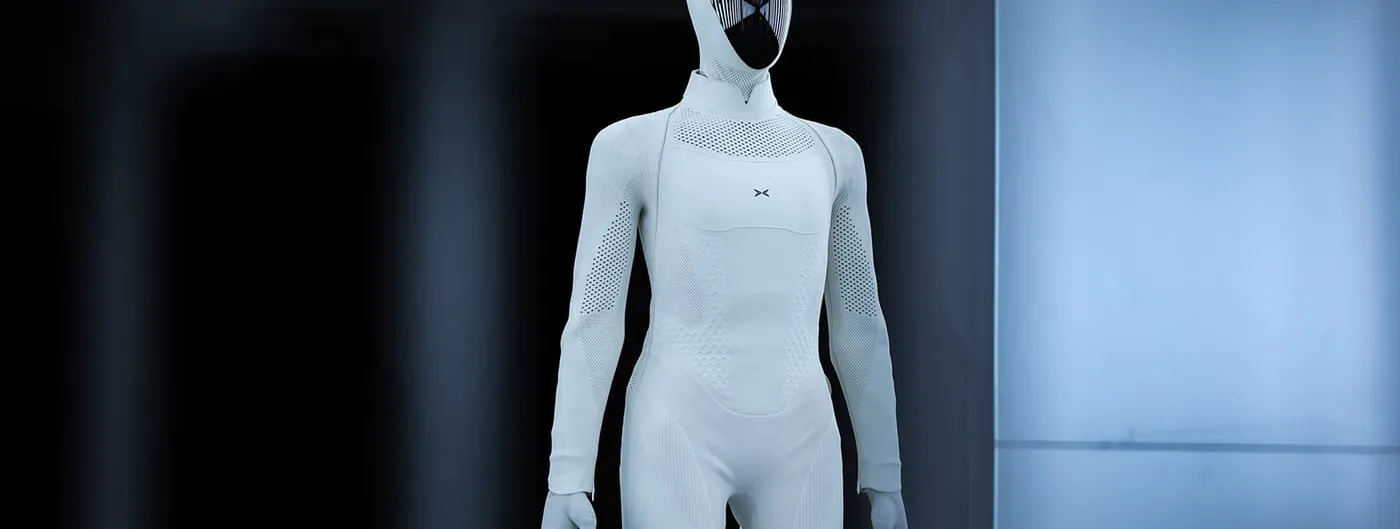 A white full-size humanoid robot in a knitted body covering with a dark reflective faceplate, standing in a dimly lit industrial hall.